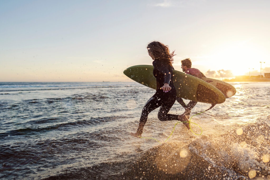 Couple rushing to catch the waves while carrying surfboards.