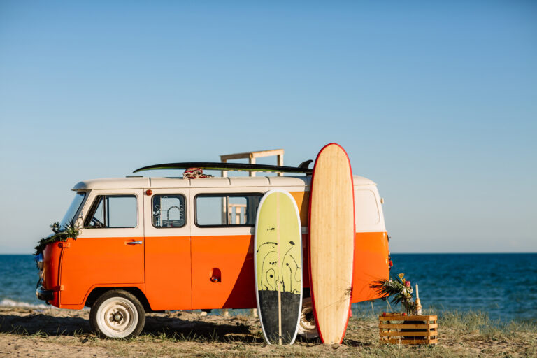 bus with a surfboard on the roof is a parked near the beach.