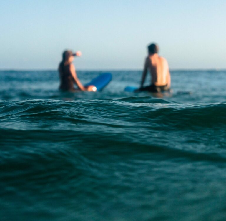 Two beginner surfers sitting on their surfboards in the ocean.