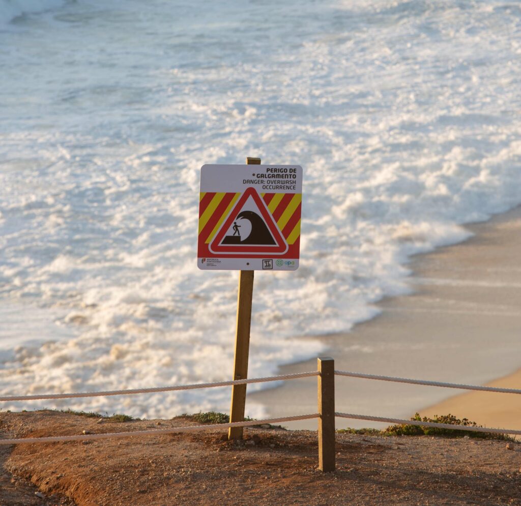 A sign by the ocean warning people about dangerous water conditions.