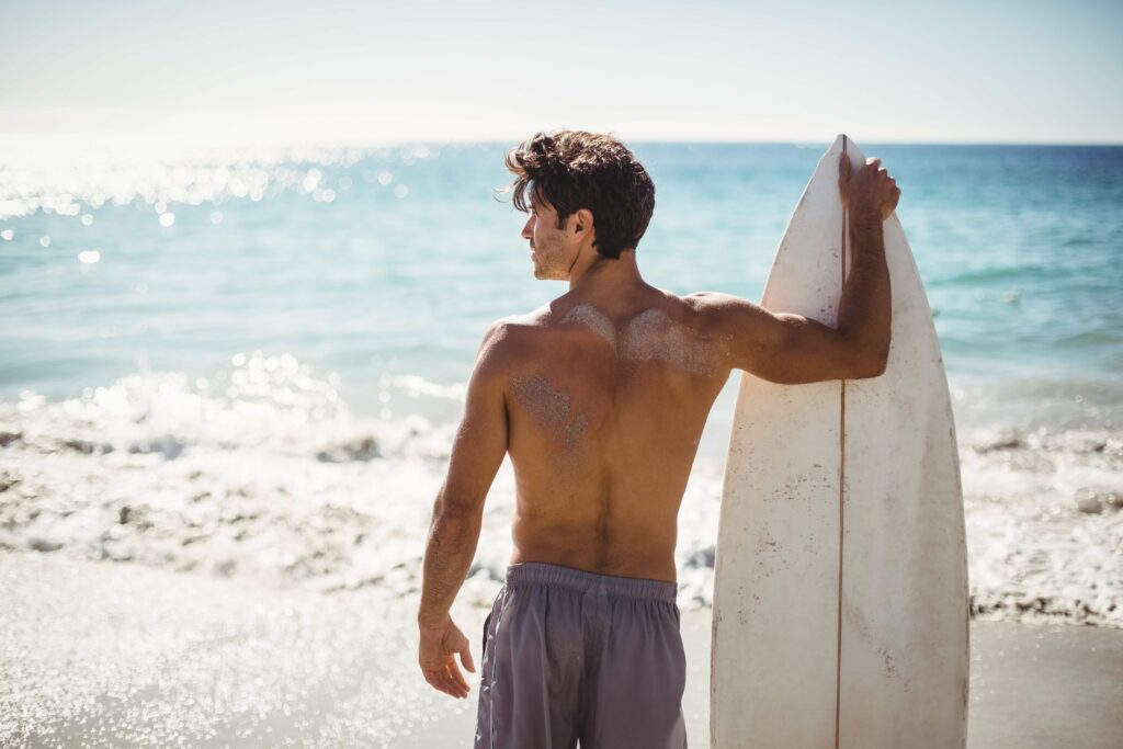 Man standing next to a surfboard that is the perfect height.