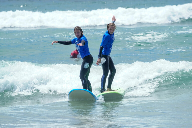 Dois alunos surfando na mesma onda e se divertindo